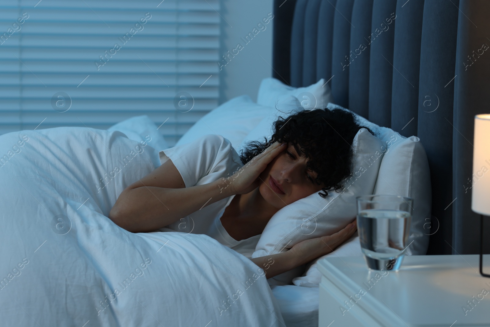 Photo of Young woman suffering from headache in bed at night