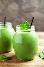 Jars of healthy green smoothie with fresh spinach on wooden table