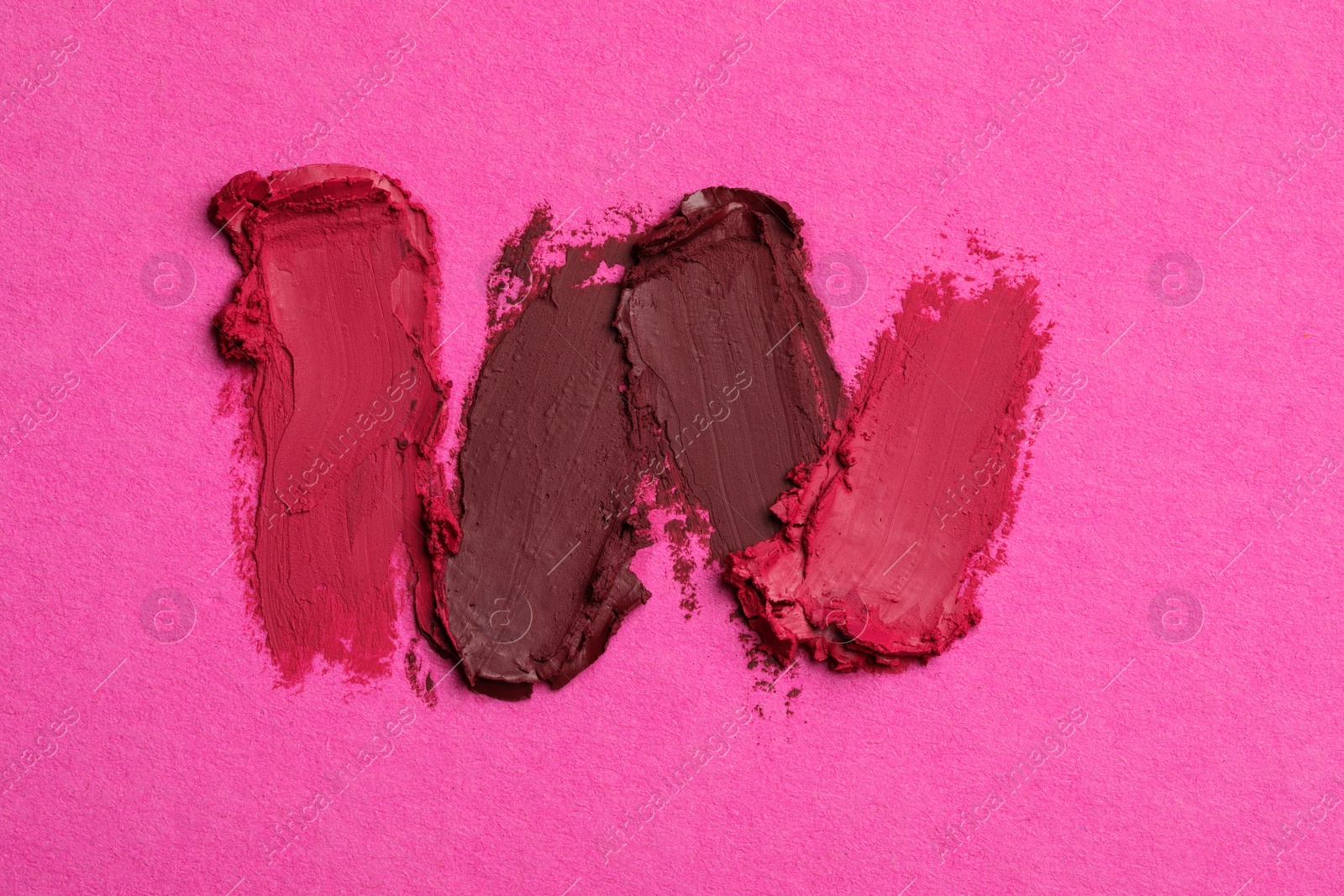 Photo of Smears of bright lipsticks on pink background, top view