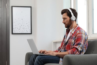 Photo of Handsome bearded man with headphones using laptop indoors