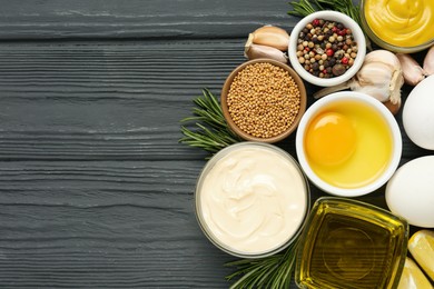 Photo of Glass bowl with fresh mayonnaise and ingredients on black wooden table, flat lay. Space for text