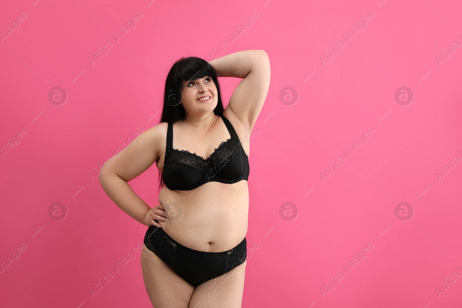 Photo of Beautiful overweight woman in black underwear on pink background, space for text. Plus-size model