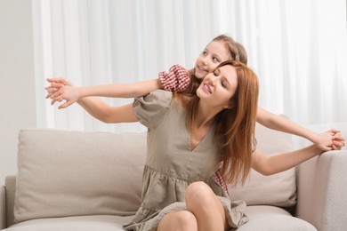 Mother with her cute daughter spending time together on sofa at home