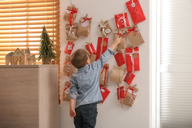 Photo of Cute little boy taking gift from Advent calendar at home, back view. Christmas tradition