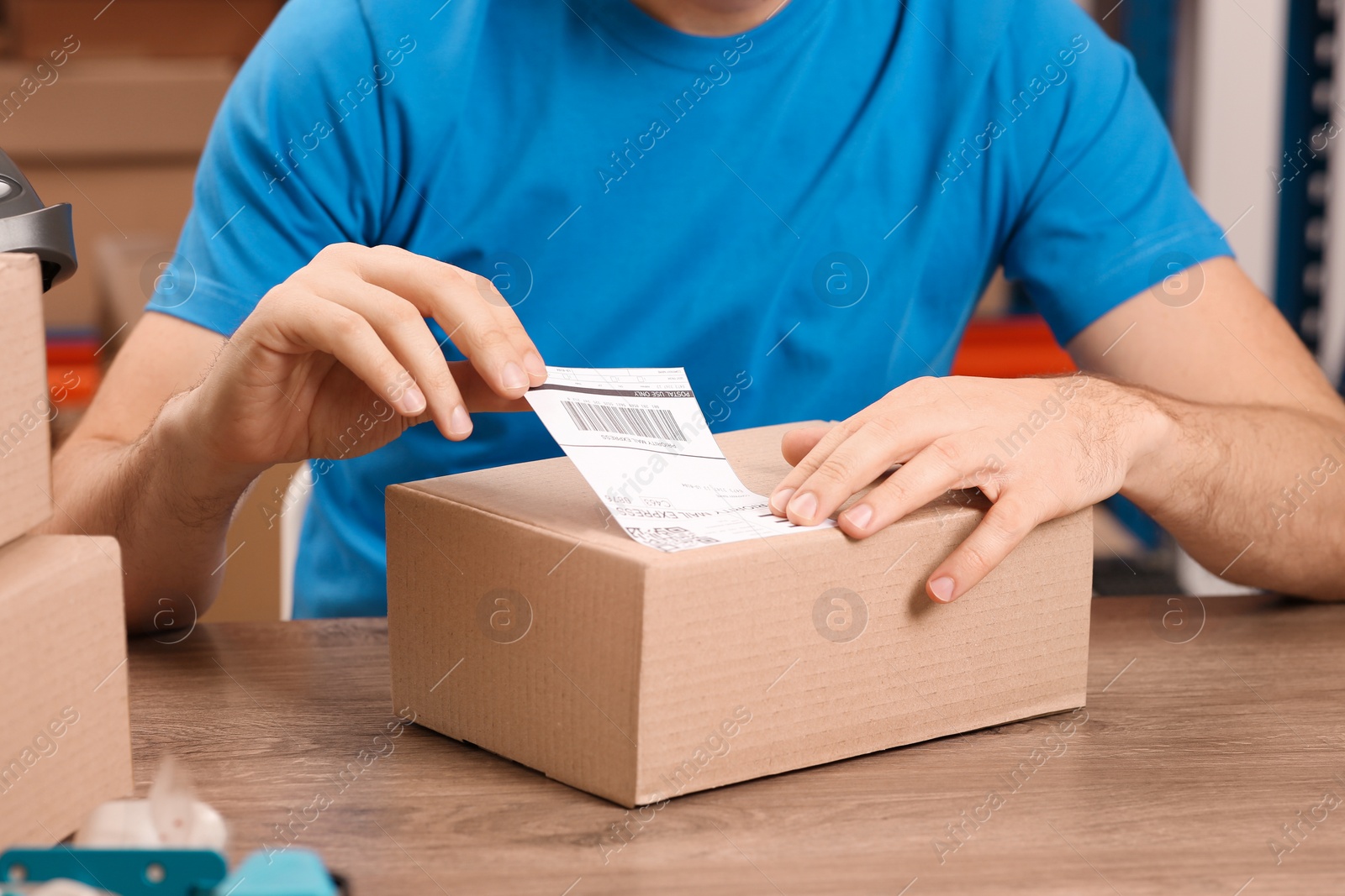 Photo of Post office worker sticking barcode on parcel at counter indoors, closeup