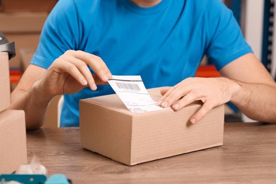 Photo of Post office worker sticking barcode on parcel at counter indoors, closeup