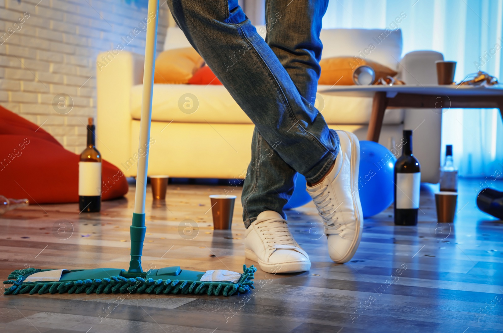 Photo of Young man with mop cleaning messy room after party, closeup of legs