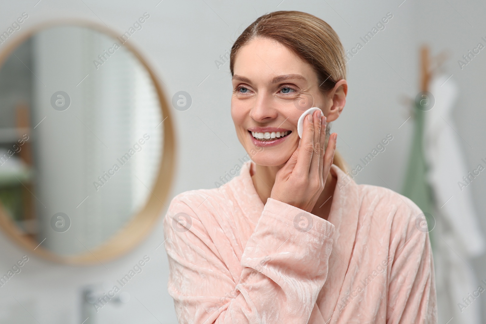 Photo of Beautiful woman removing makeup with cotton pad indoors, space for text