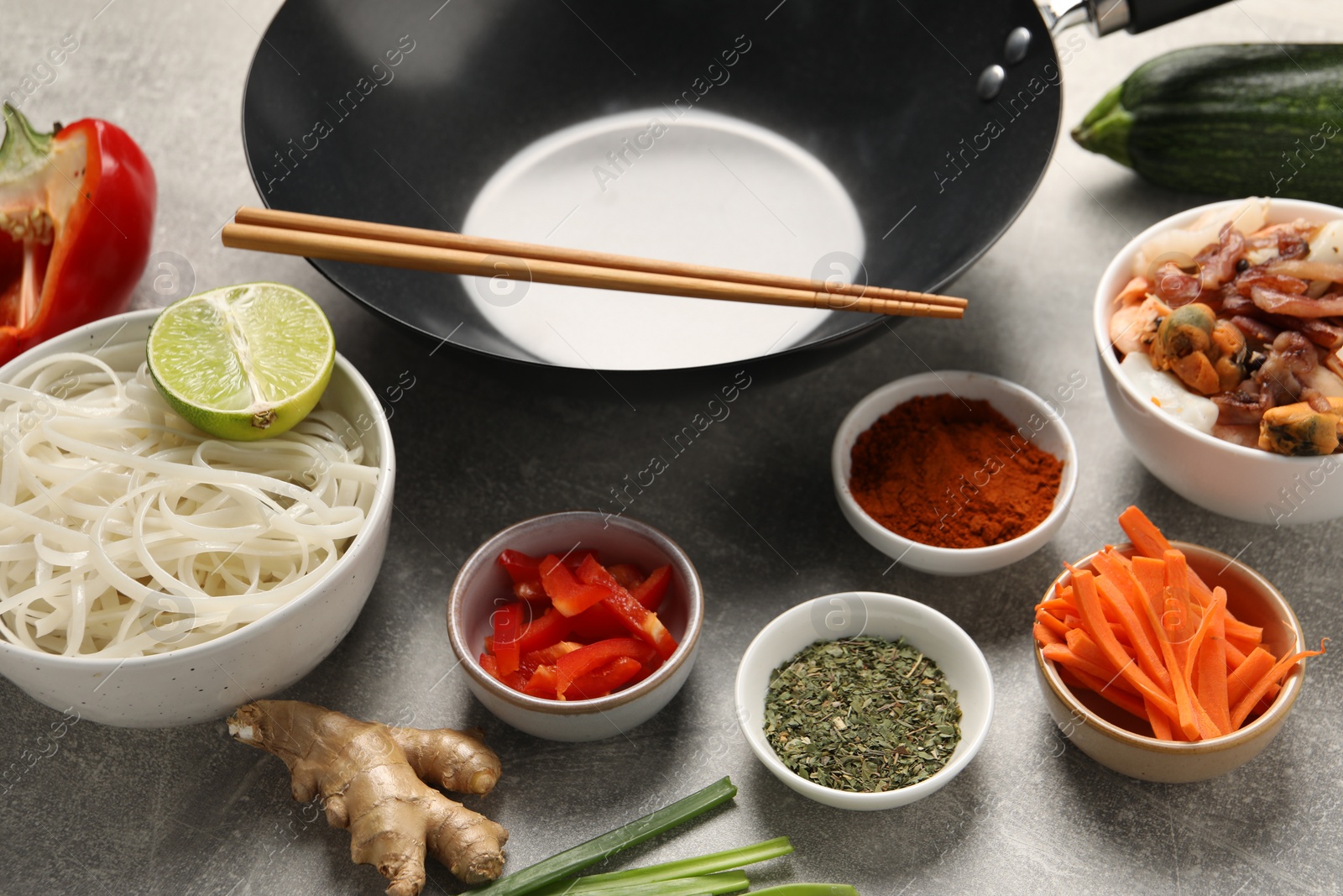 Photo of Black wok, spices and products on grey textured table, closeup