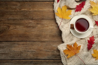 Cup of hot tea, sweater and autumn leaves on wooden table, flat lay. Space for text