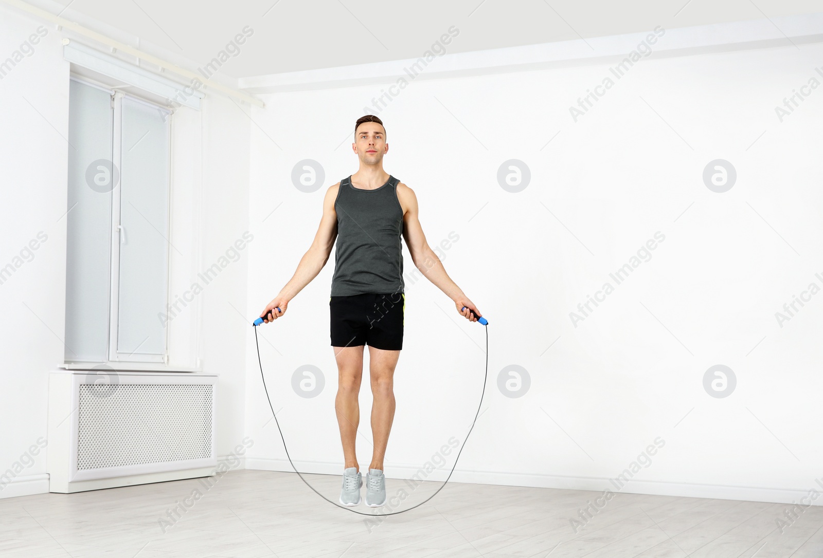 Photo of Full length portrait of young sportive man training with jump rope in light room