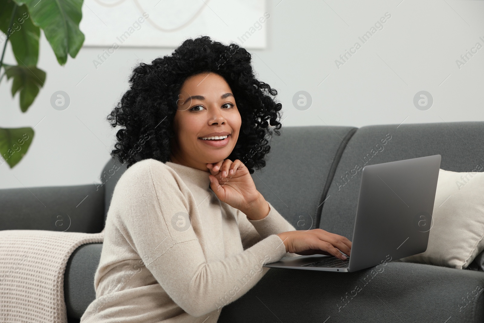 Photo of Happy young woman using laptop on sofa indoors