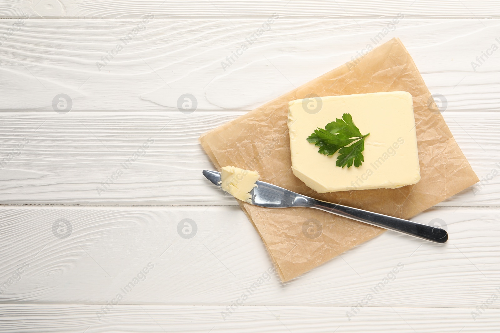 Photo of Tasty butter and knife on white wooden table, top view. Space for text