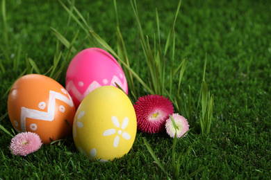 Photo of Colorful Easter eggs and daisy flowers in green grass. Space for text