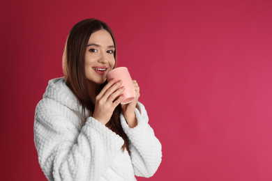 Photo of Young woman in bathrobe with cup of morning drink on crimson background, space for text