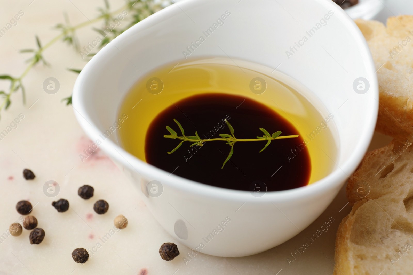 Photo of Bowl of organic balsamic vinegar with oil, spices and bread slices on beige table, closeup