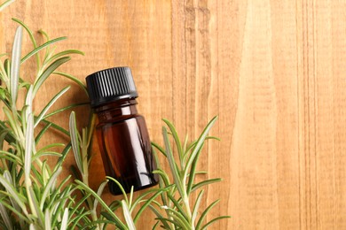 Photo of Bottle of rosemary oil and fresh twigs on wooden table, flat lay. Space for text