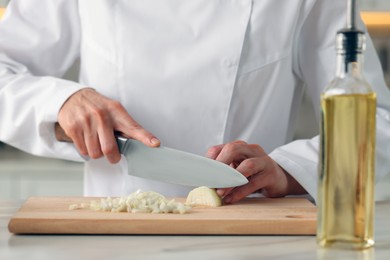 Photo of Professional chef cutting onion at white marble table indoors, closeup