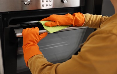 Woman with microfiber cloth cleaning electric oven in kitchen, closeup