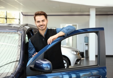 Young man near new car in dealership