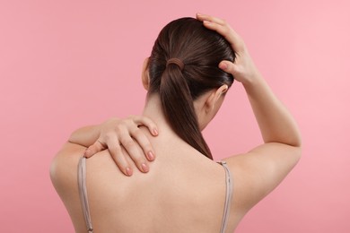 Woman touching her neck and head on pink background, back view