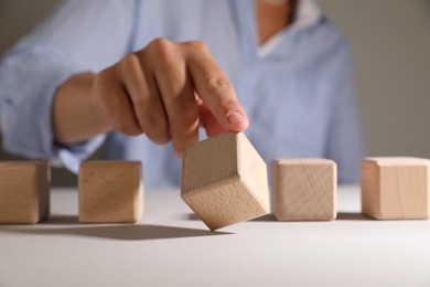 Woman choosing wooden cube among others at white table, closeup