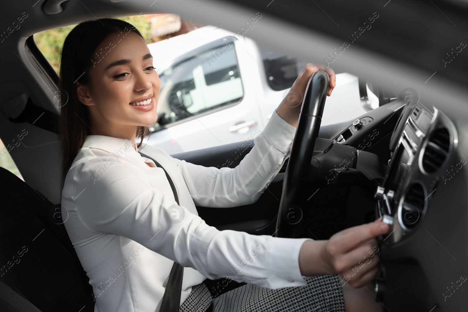 Photo of Listening to radio while driving. Beautiful young woman turning volume button on vehicle audio in car