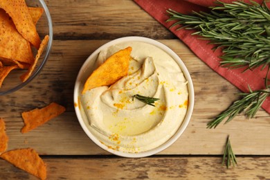 Delicious hummus with nachos and rosemary on wooden table, flat lay