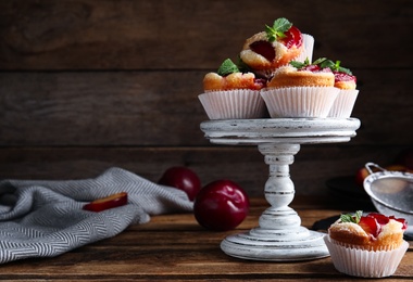 Photo of Delicious sweet cupcakes with plums on wooden table. Space for text