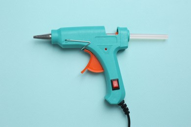Glue gun with stick on turquoise background, top view