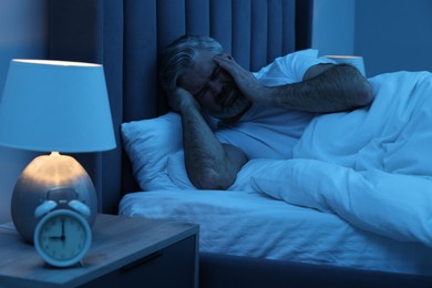 Photo of Mature man suffering from headache in bed at night