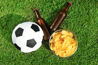 Photo of Soccer ball with beverage and chips on green football field grass, flat lay