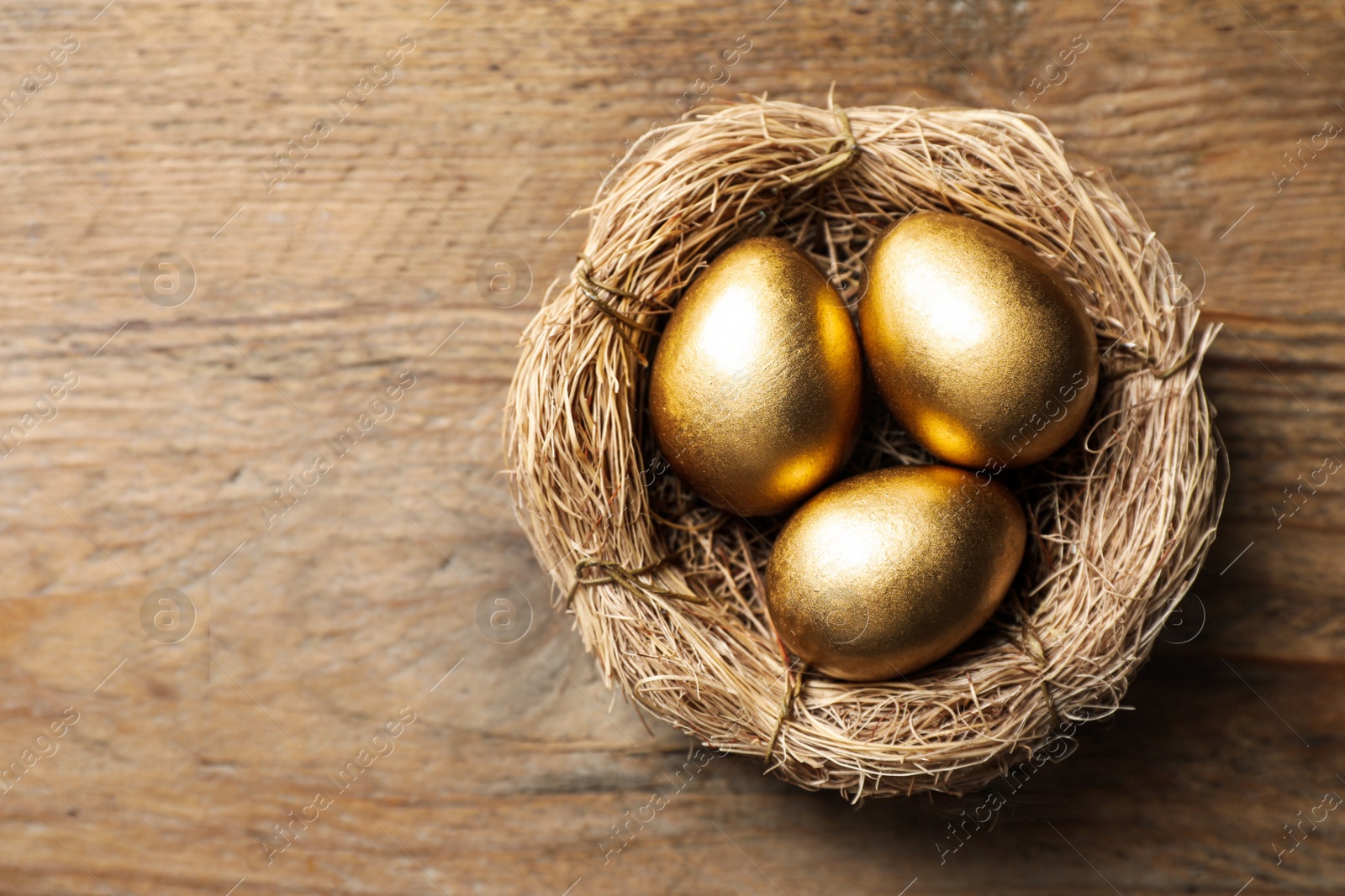 Photo of Nest with golden eggs on wooden table, top view. Space for text