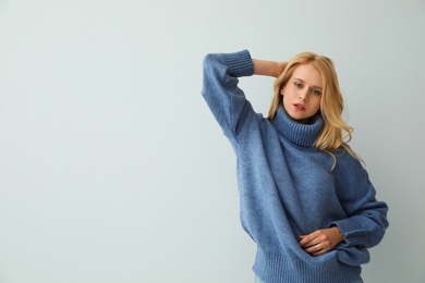 Photo of Beautiful young woman wearing warm blue sweater on light background. Space for text