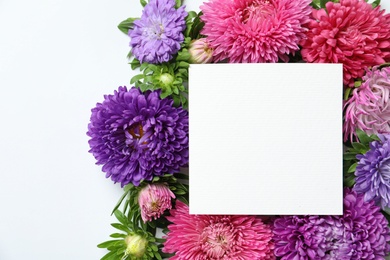 Beautiful aster flowers with sheet of paper on white background, top view. Space for text