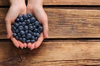 Photo of Woman with heap of tasty blueberries on wooden background, top view. Space for text