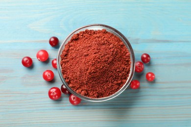 Cranberry powder in bowl and fresh berries on light blue wooden table, top view