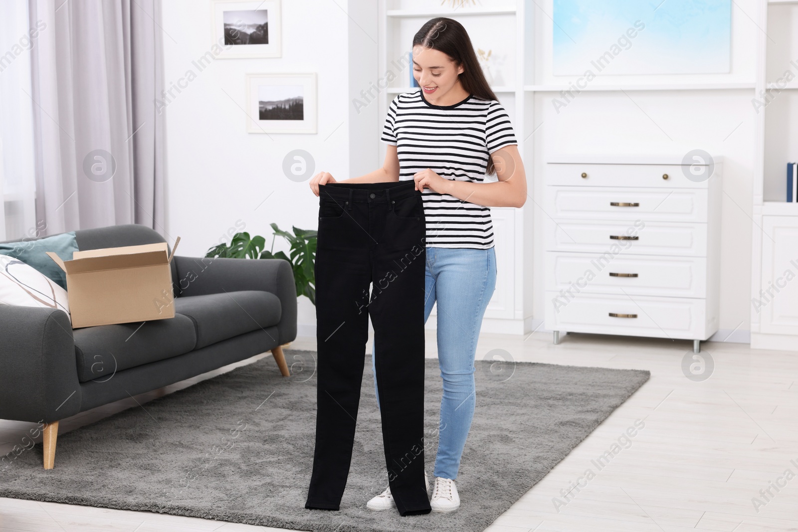 Photo of Happy woman with stylish black jeans at home. Online shopping