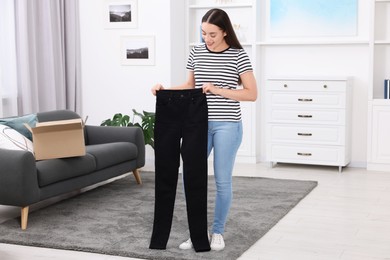 Photo of Happy woman with stylish black jeans at home. Online shopping