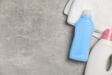 Bottles of laundry detergents and clean towel on light grey table, flat lay. Space for text