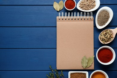 Blank recipe book and different spices on blue wooden table, flat lay. Space for text