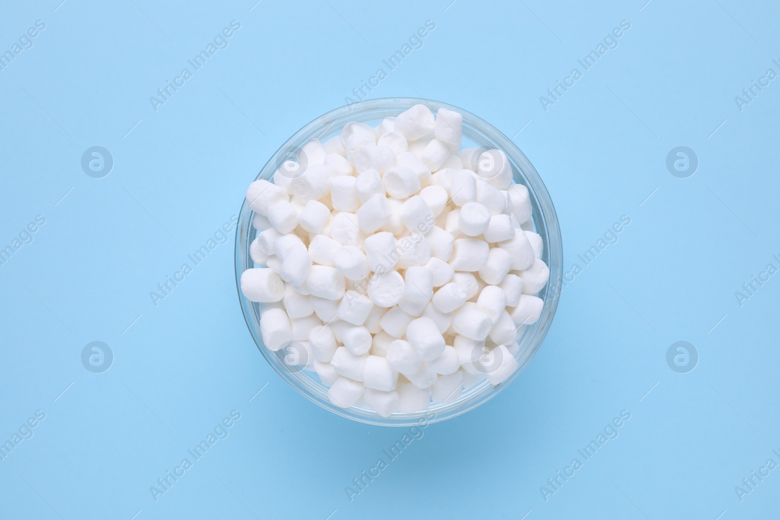 Photo of Bowl with delicious marshmallows on light blue background, top view