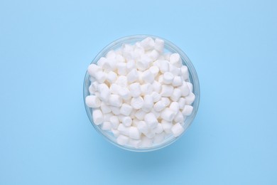 Bowl with delicious marshmallows on light blue background, top view