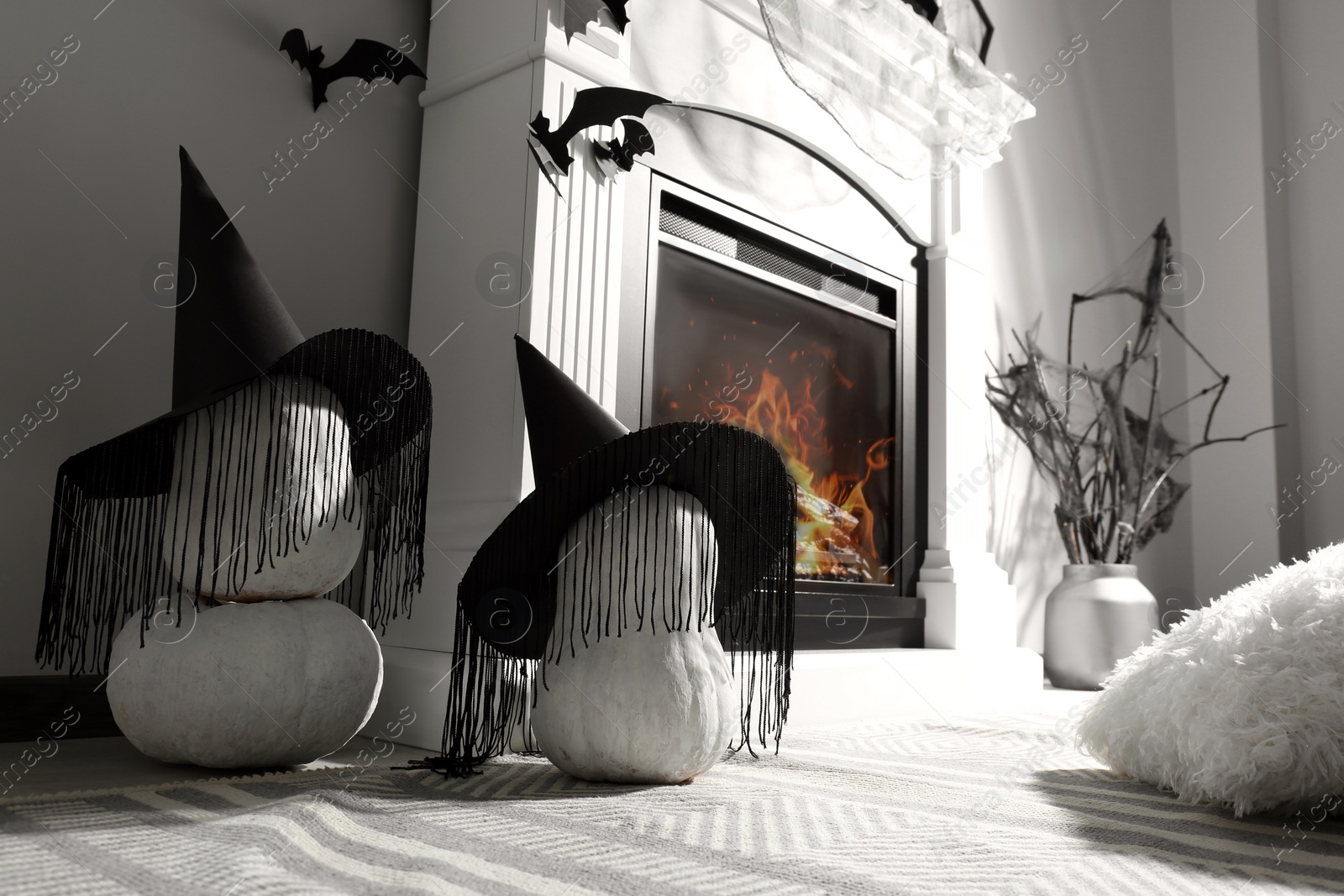 Photo of Beautiful black witch hats on pumpkins near fireplace indoors. Halloween celebration