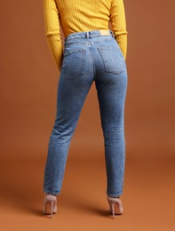 Woman in stylish jeans on brown background, closeup