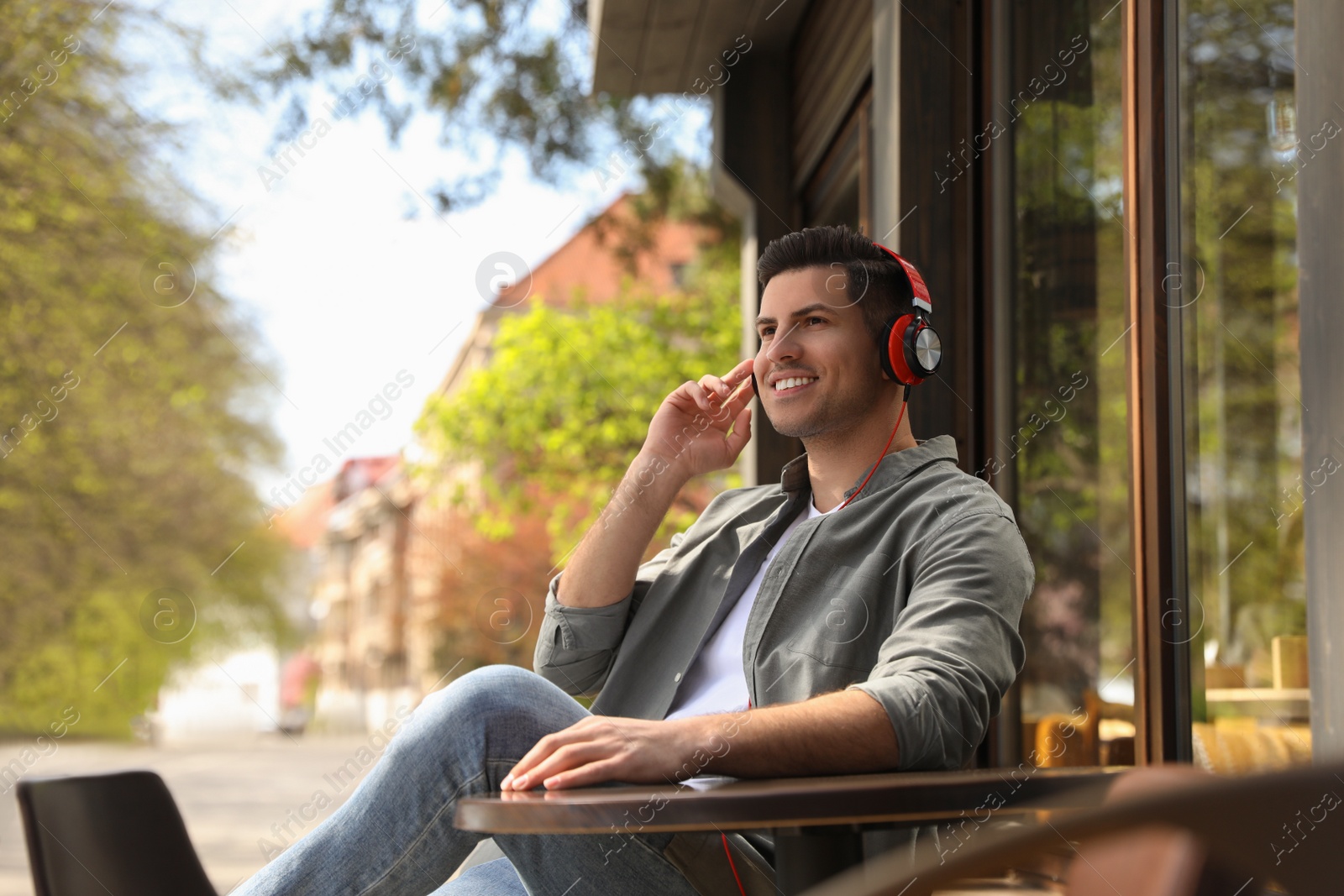 Photo of Handsome man with headphones listening to music in outdoor cafe, space for text