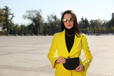 Beautiful young woman with stylish waist bag on city street, space for text