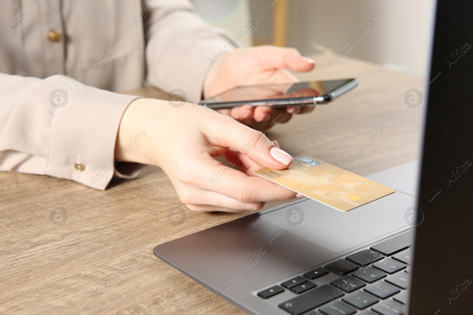 Photo of Online payment. Woman using smartphone and credit card near laptop at wooden table indoors, closeup