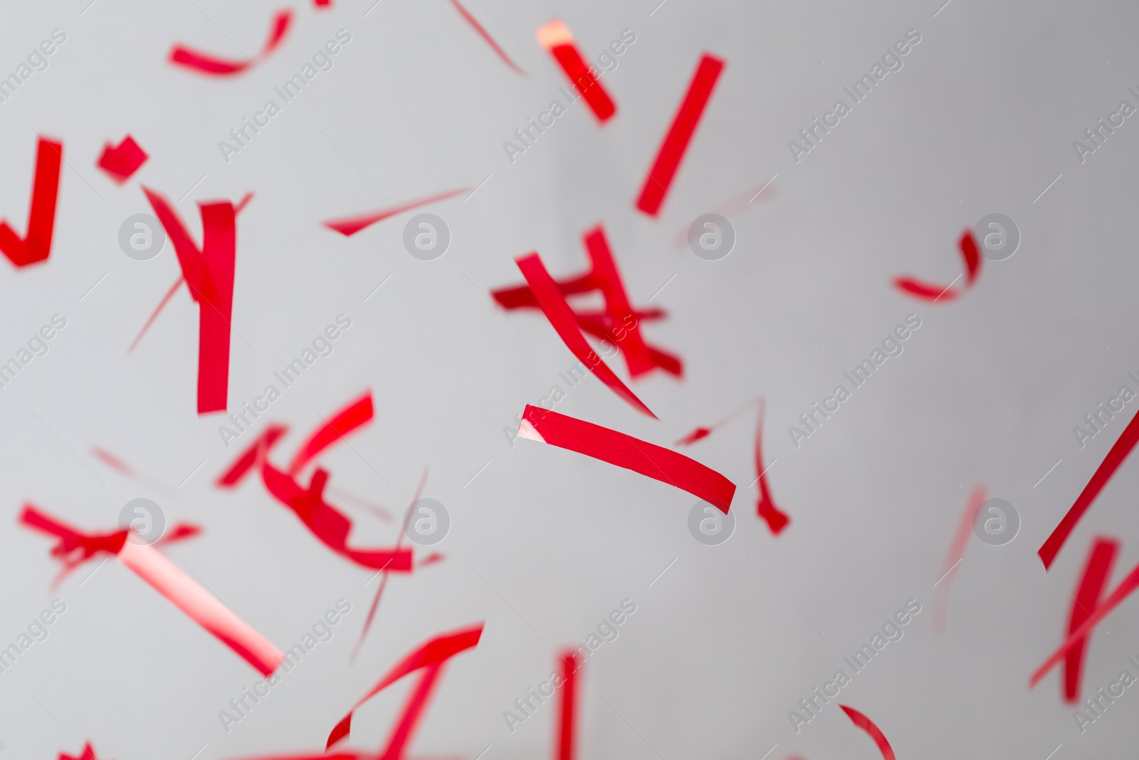 Photo of Shiny red confetti falling down on light grey background