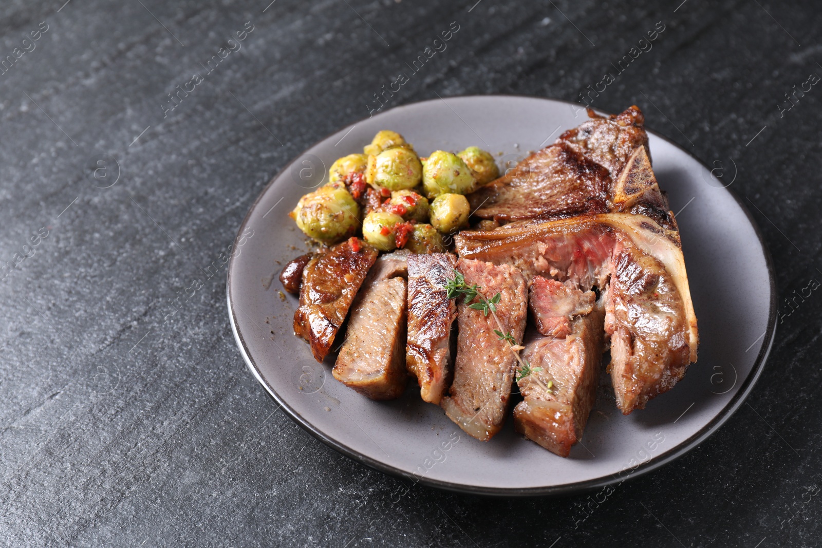 Photo of Delicious fried beef meat, vegetables and thyme on black table